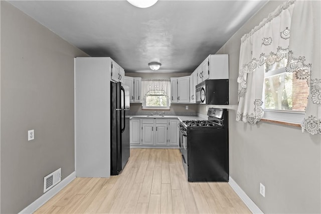 kitchen featuring a sink, light wood finished floors, baseboards, visible vents, and black appliances