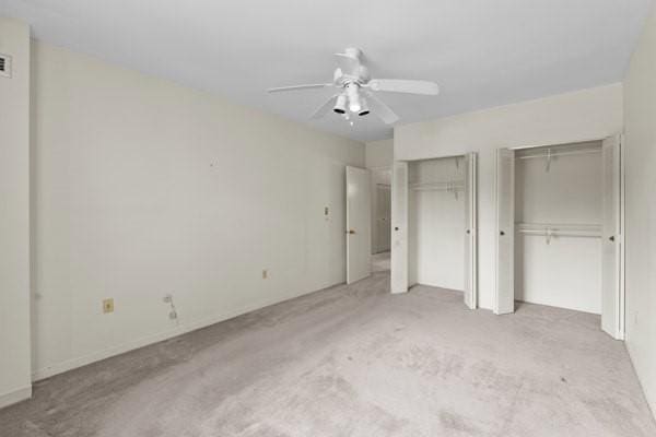 unfurnished bedroom with a ceiling fan, carpet, and two closets