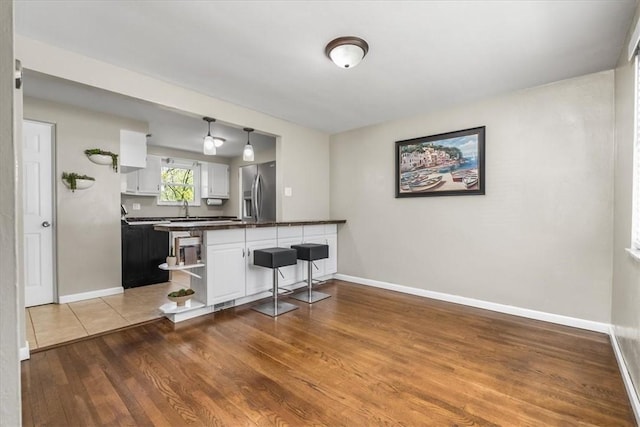 kitchen with dark countertops, open shelves, white cabinets, a peninsula, and stainless steel fridge