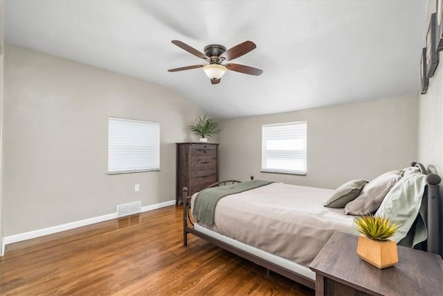 bedroom featuring a ceiling fan, visible vents, vaulted ceiling, wood finished floors, and baseboards