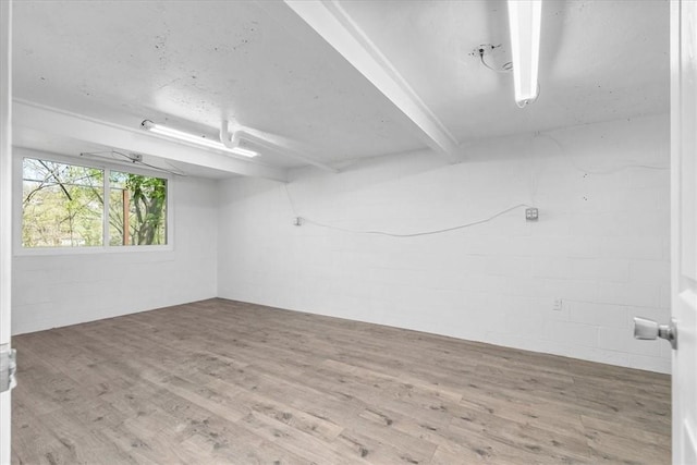 spare room with beam ceiling, wood finished floors, and concrete block wall