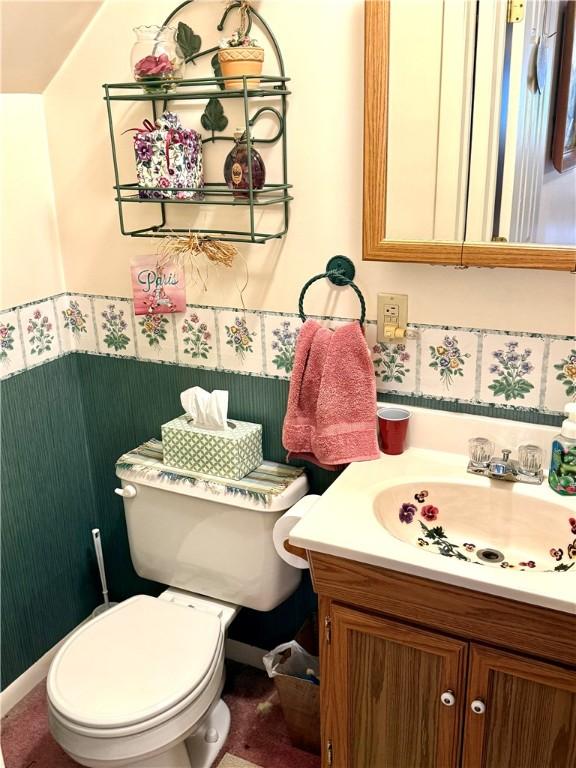 half bath featuring vanity, a wainscoted wall, and toilet