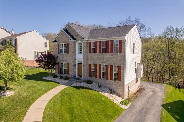 colonial house featuring a shingled roof, a front yard, aphalt driveway, and brick siding