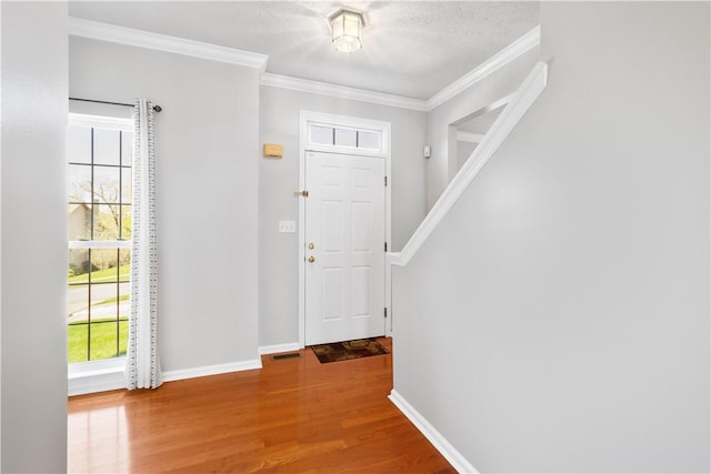 foyer entrance featuring crown molding, baseboards, wood finished floors, and visible vents
