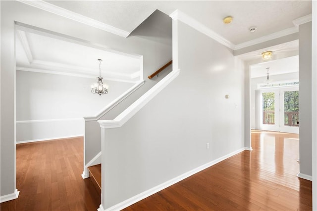 corridor with ornamental molding, wood finished floors, baseboards, stairway, and a chandelier