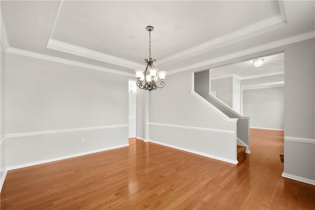 unfurnished dining area featuring wood finished floors, stairway, baseboards, a chandelier, and a tray ceiling