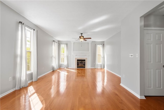 unfurnished living room featuring baseboards, ceiling fan, light wood finished floors, and a tile fireplace