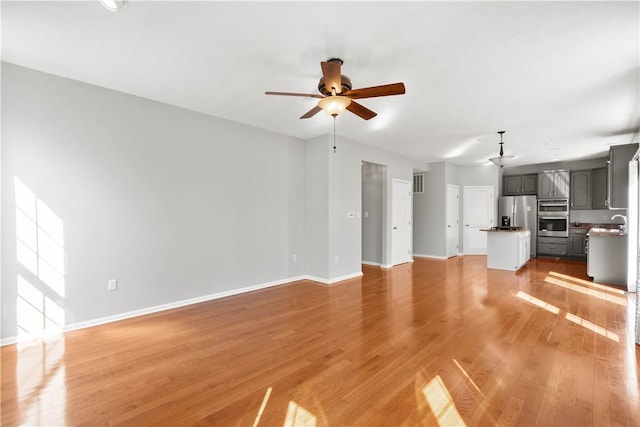 unfurnished living room with baseboards, ceiling fan, light wood-style flooring, and visible vents