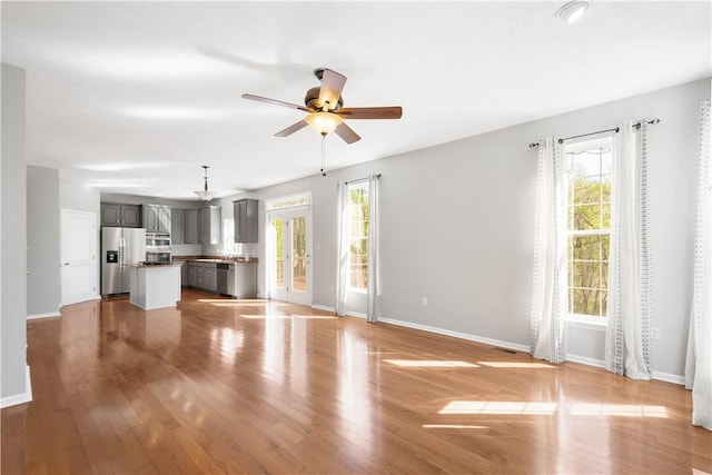 unfurnished living room with baseboards, a healthy amount of sunlight, and ceiling fan