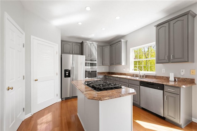 kitchen with stainless steel appliances, gray cabinetry, light stone counters, and light wood-style floors