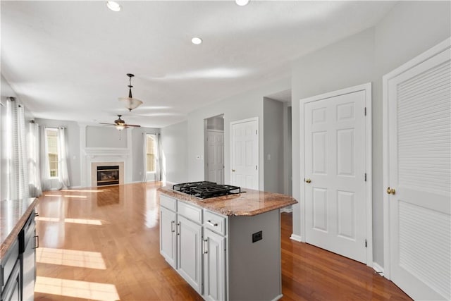 kitchen featuring gas cooktop, a ceiling fan, a center island, a glass covered fireplace, and light wood-style flooring