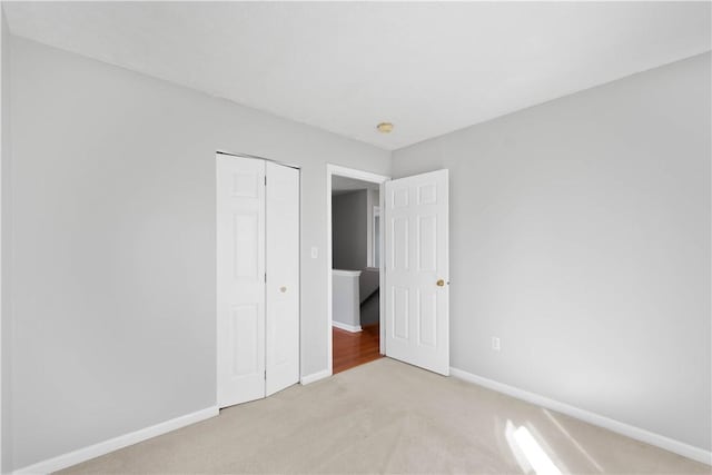 unfurnished bedroom featuring baseboards, light colored carpet, and a closet