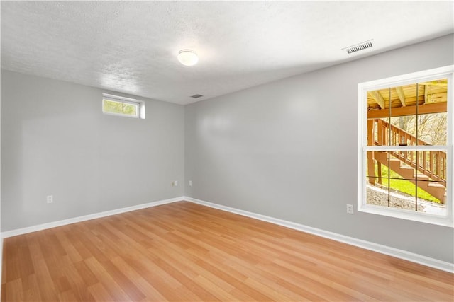 spare room featuring a textured ceiling, baseboards, visible vents, and light wood-style flooring