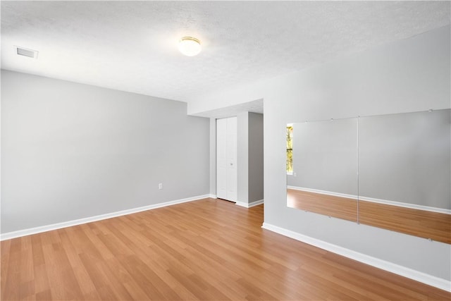 spare room featuring visible vents, a textured ceiling, baseboards, and wood finished floors