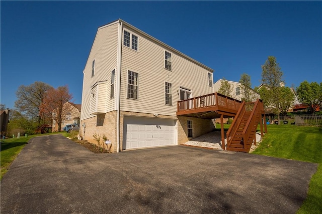 rear view of house with driveway, a deck, an attached garage, a yard, and stairway