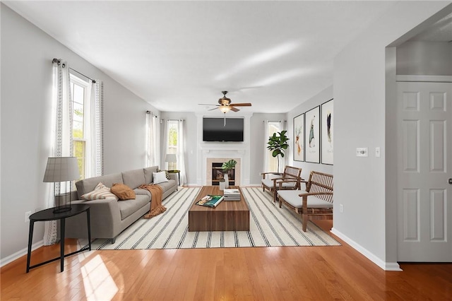 living area featuring baseboards, light wood finished floors, ceiling fan, and a tile fireplace