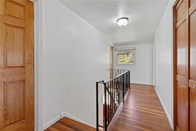 corridor featuring baseboards, wood finished floors, and an upstairs landing