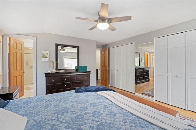 bedroom with multiple closets, lofted ceiling, ceiling fan, light wood-type flooring, and connected bathroom