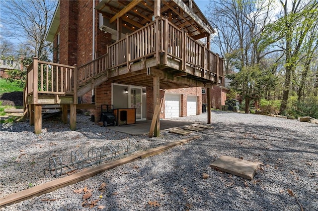 rear view of property with brick siding, an attached garage, a wooden deck, and gravel driveway