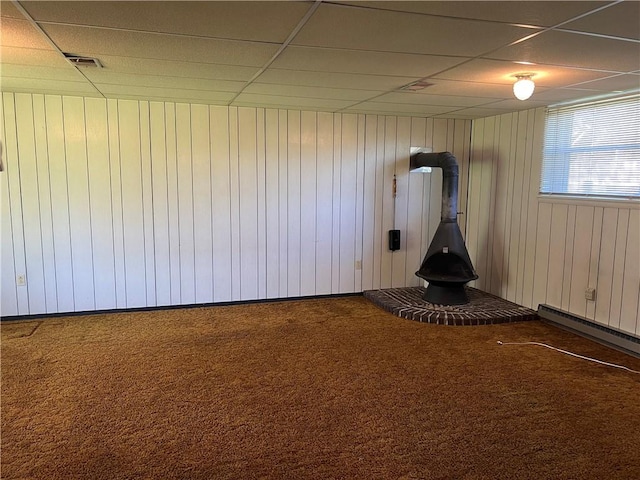 interior space featuring wooden walls, carpet floors, a wood stove, and a paneled ceiling