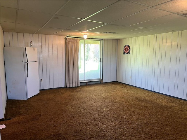 unfurnished room featuring dark carpet, a paneled ceiling, and wooden walls