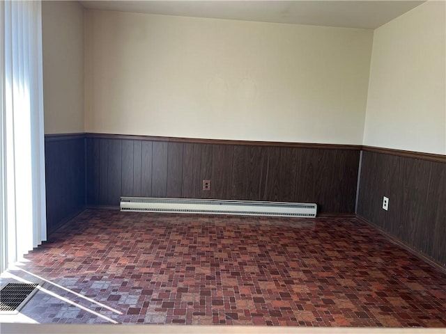 empty room featuring wood walls, a baseboard heating unit, wainscoting, and baseboards