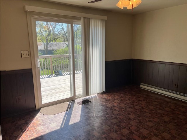 spare room featuring visible vents, wood walls, wainscoting, a baseboard heating unit, and a ceiling fan