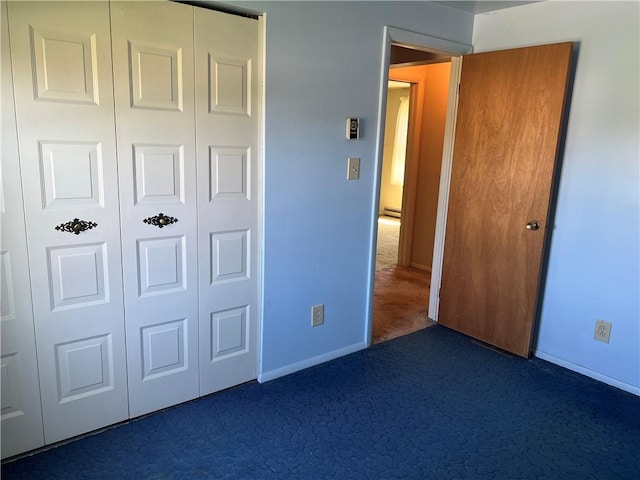 unfurnished bedroom featuring baseboards, baseboard heating, a closet, and dark carpet
