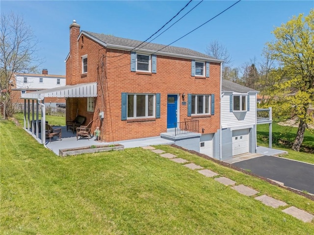 rear view of house featuring driveway, a chimney, brick siding, a yard, and an attached garage