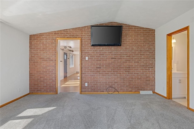 carpeted spare room with baseboards, lofted ceiling, and brick wall