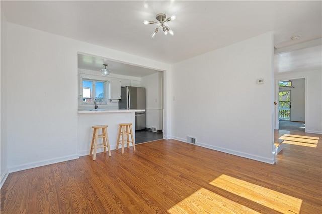 unfurnished living room featuring visible vents, baseboards, wood finished floors, and a notable chandelier