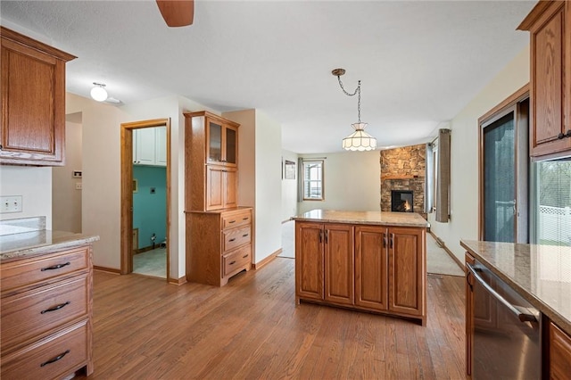 kitchen featuring stainless steel dishwasher, brown cabinetry, wood finished floors, and a fireplace