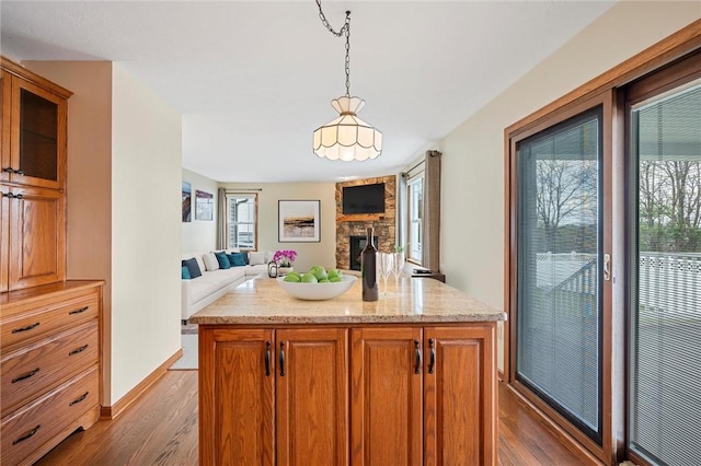 kitchen with dark wood-style flooring, decorative light fixtures, a center island, a fireplace, and brown cabinets