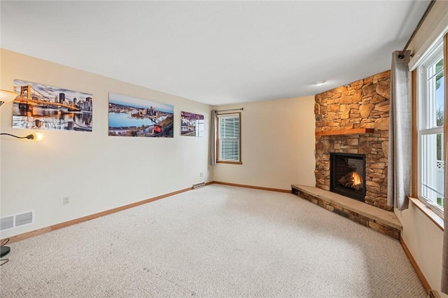 unfurnished living room with baseboards, visible vents, a stone fireplace, and carpet