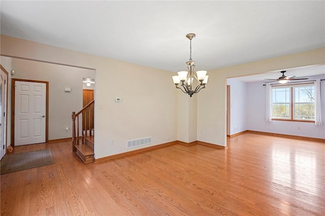 spare room featuring visible vents, light wood-type flooring, stairway, baseboards, and ceiling fan with notable chandelier