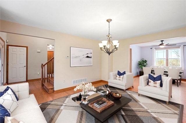 living area featuring visible vents, baseboards, stairway, light wood-type flooring, and a chandelier
