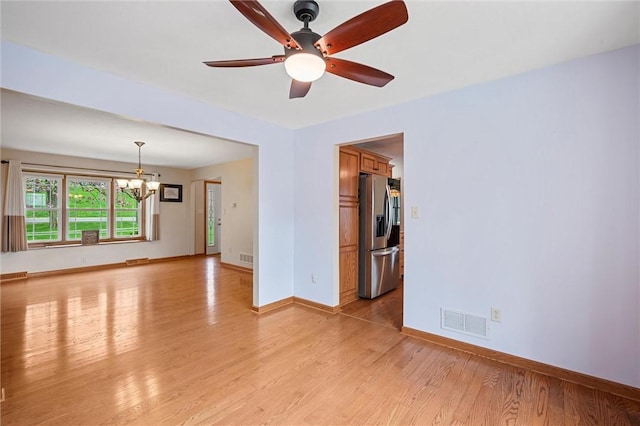 unfurnished room with visible vents, light wood-style flooring, ceiling fan with notable chandelier, and baseboards