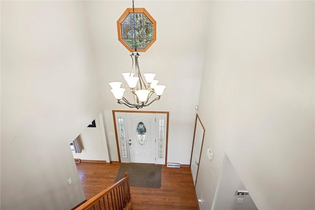 entrance foyer featuring an inviting chandelier, visible vents, a towering ceiling, wood finished floors, and baseboards