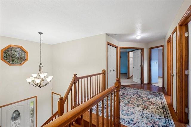 hall featuring baseboards, a notable chandelier, wood finished floors, and an upstairs landing