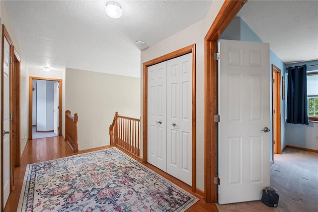hall featuring baseboards, a textured ceiling, wood finished floors, and an upstairs landing