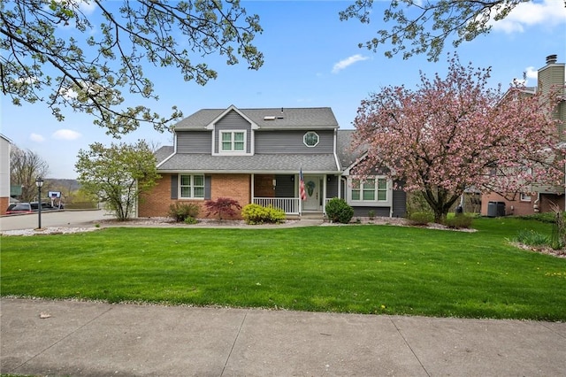 traditional-style home with roof with shingles, a porch, brick siding, and a front yard