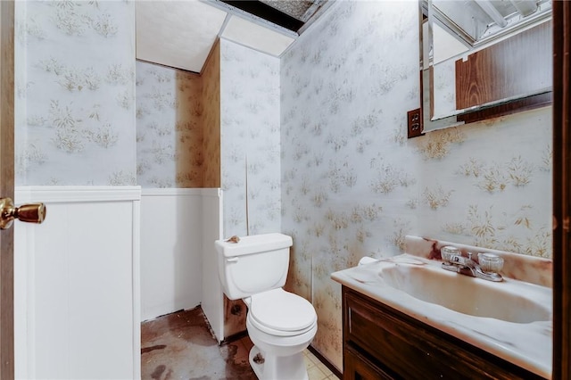 bathroom with toilet, wallpapered walls, wainscoting, and vanity