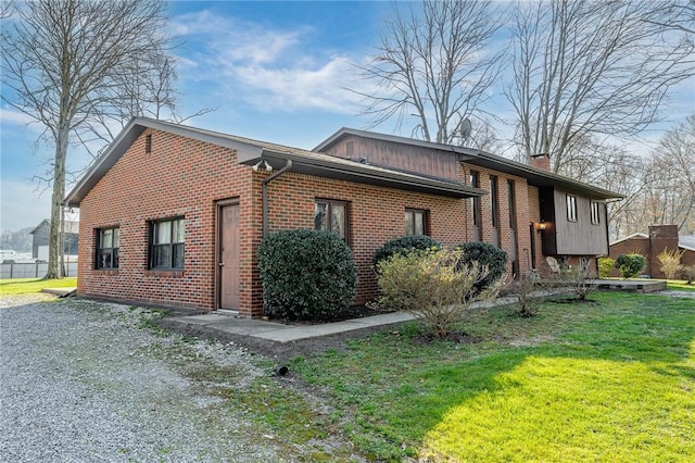 view of side of property featuring brick siding, a yard, and a chimney