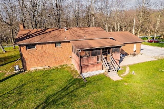 back of property with a lawn, brick siding, a chimney, and stairs
