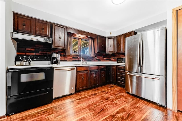 kitchen with dark brown cabinetry, appliances with stainless steel finishes, light wood-type flooring, a sink, and light countertops