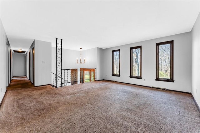 unfurnished living room with baseboards, plenty of natural light, carpet, and a chandelier