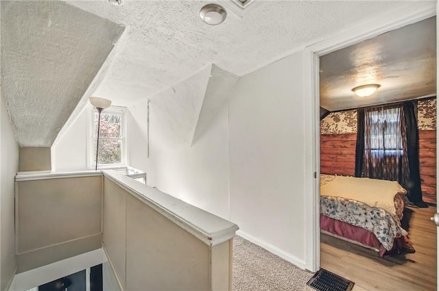 corridor featuring baseboards, vaulted ceiling, and a textured ceiling