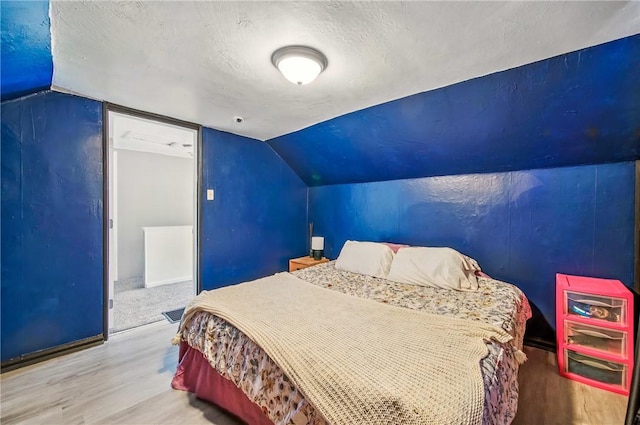 bedroom featuring baseboards, a textured ceiling, vaulted ceiling, and wood finished floors