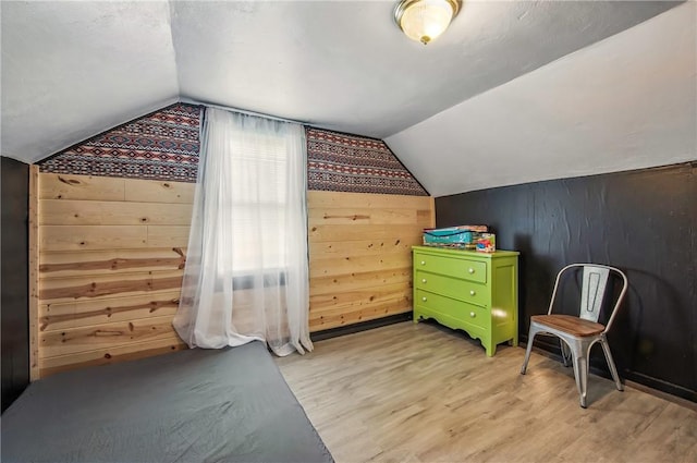 additional living space with light wood finished floors, wooden walls, and vaulted ceiling