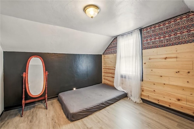 bedroom with wood walls, wood finished floors, and vaulted ceiling